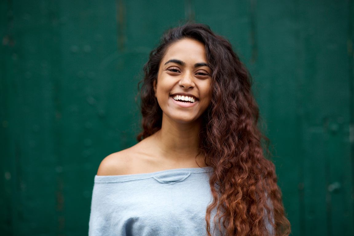 Close up Beautiful Young Indian Woman with Long Hair Smiling against Green Background